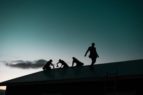 Emergency roofing team repairing a storm-damaged commercial flat roof at dusk.