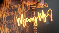 A glowing 'Will U Marry Me' neon sign hanging amidst tropical flowers on the beach.