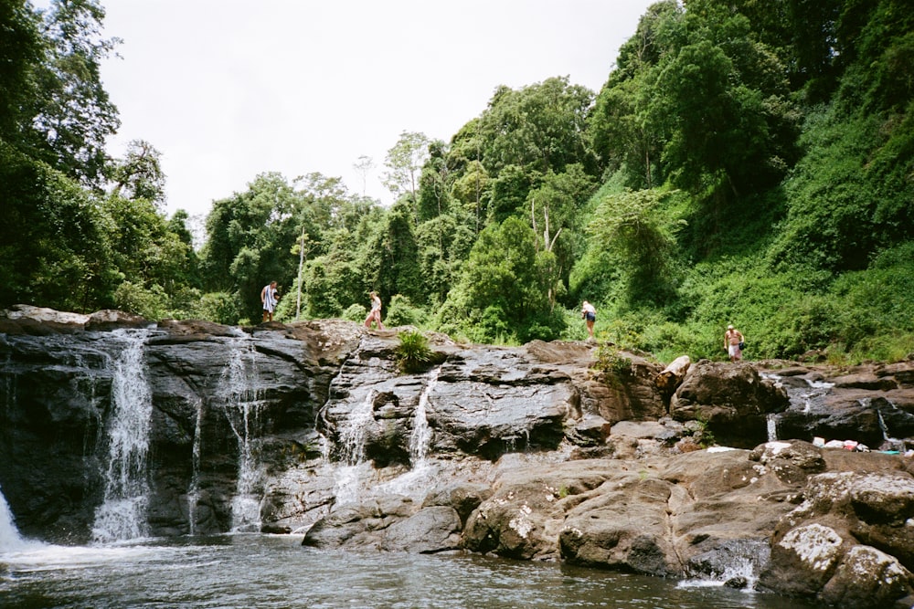 a group of people standing on rocks by a waterfall