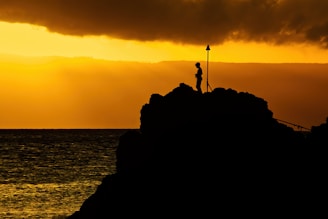 a lone man stands atop black rock