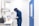 A person wearing a blue protective suit and mask is working in a laboratory setting. They are handling petri dishes on a counter with a digital display and laboratory equipment nearby. The room has clean, white walls and a blue door.