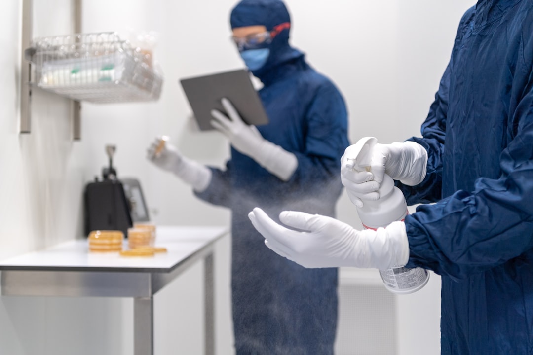 a couple of people wearing gloves and masks and gloves, Laboratory technician disinfecting hands with disinfection spray