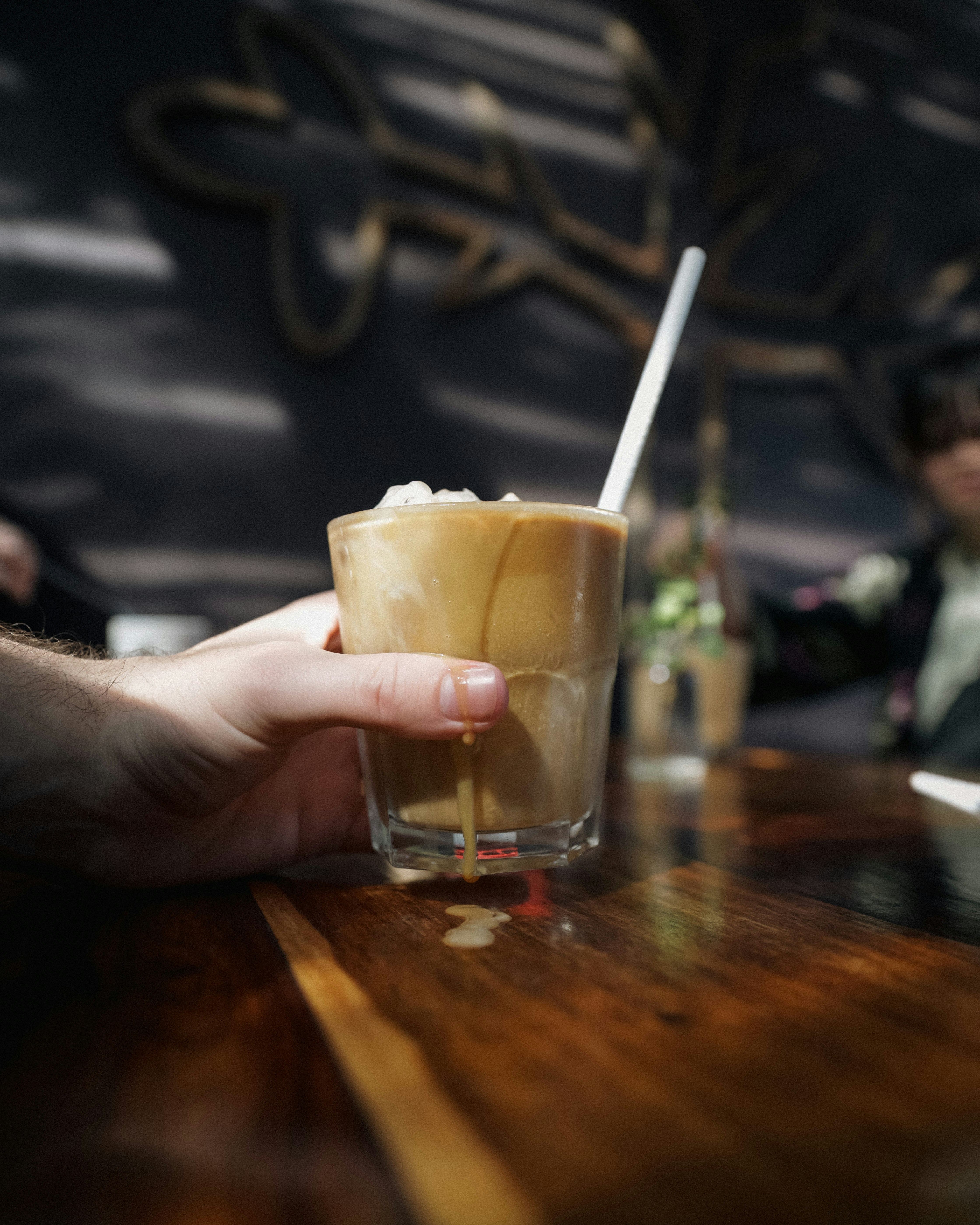 Hand holding a cold coffee with ice and straw.
