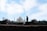A silhouetted man and child walk on a path in the foreground, with the iconic white marble structure of the Taj Mahal prominently visible in the background. The sky is partly cloudy, creating a serene and tranquil atmosphere.