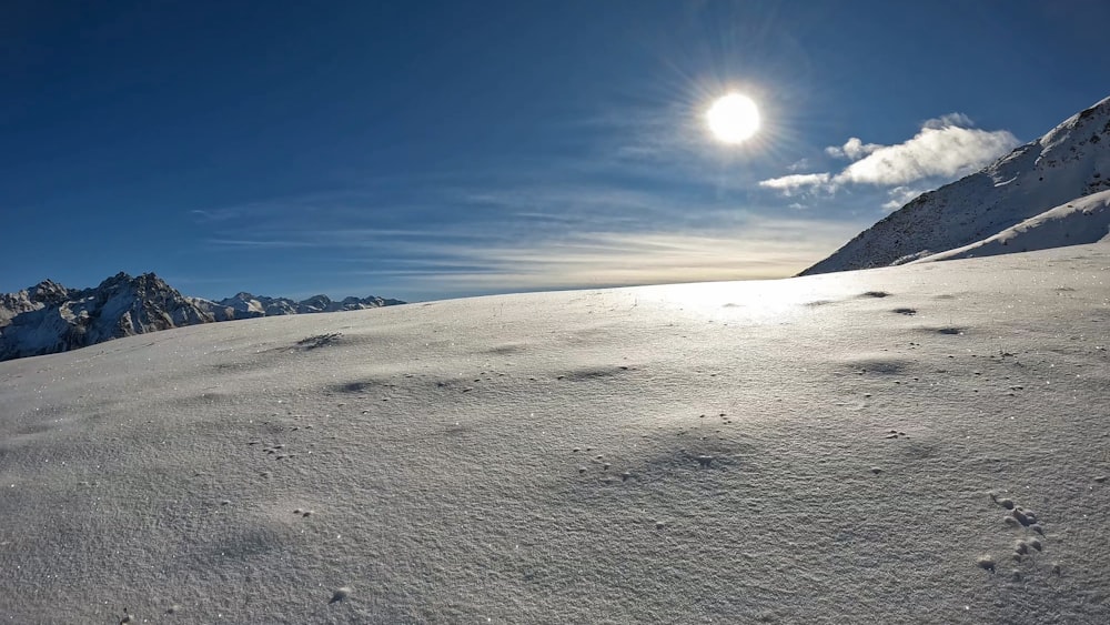 a snowy landscape with mountains and the sun in the sky