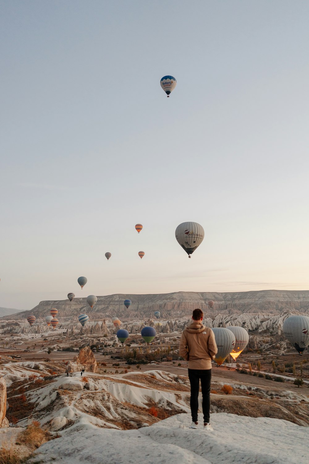 Una persona parada en una colina con globos aerostáticos en el aire