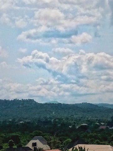 A panoramic view of lush green residential plots surrounded by rolling hills and clear skies.