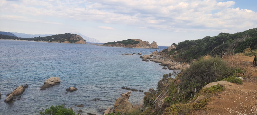 una playa rocosa con un cuerpo de agua y colinas al fondo