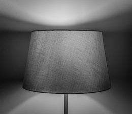 A close-up of a fabric lampshade with a subtle texture, illuminated softly, creating a play of light and shadow on the wall behind.