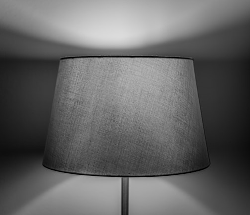 A close-up of a fabric lampshade with a subtle texture, illuminated softly, creating a play of light and shadow on the wall behind.