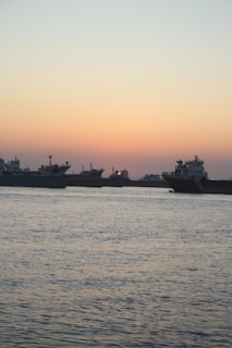 A panoramic view of a fleet of ships anchored near the Malaysian coastline at sunset.