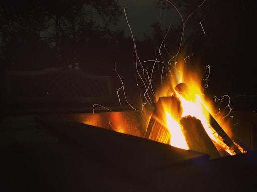 A cozy outdoor scene featuring a heartfuego wood-burning stove glowing warmly beside a tent at dusk.