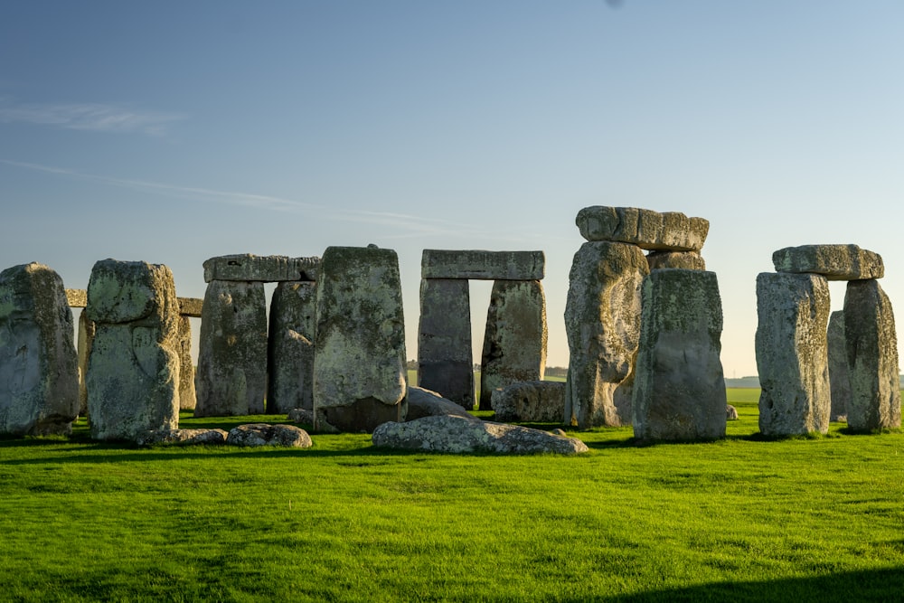 a group of rocks in a grassy field with Stonehenge in the background