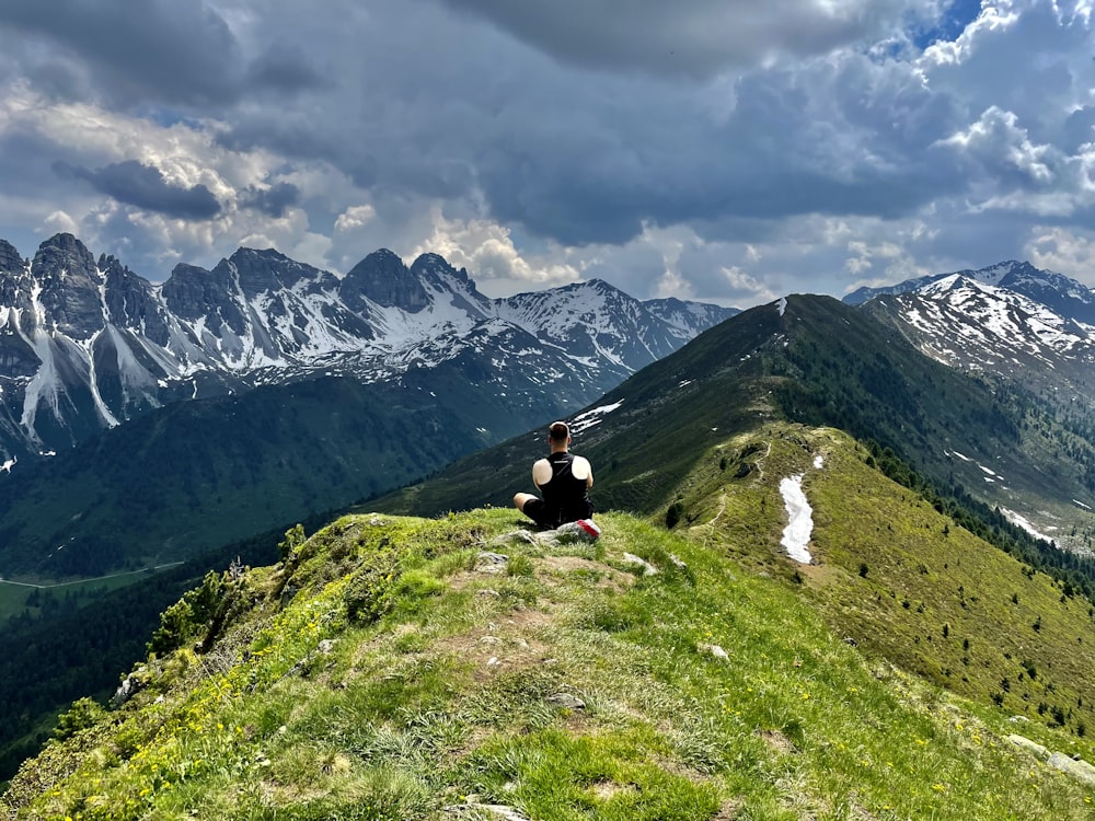 a person sitting on a grassy hill with mountains in the background