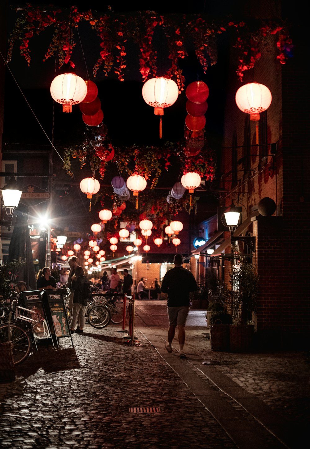 a group of people walking down a sidewalk with lanterns from the ceiling