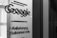 A grayscale photo showing the word 'Google' along with text in English and German on a glass surface, possibly a door or window. The surrounding area appears out of focus, emphasizing the text.