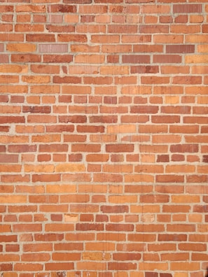 A textured surface composed of evenly sized rectangular bricks. The bricks display a range of reddish-brown hues with some variation in shade, separated by slightly faded mortar lines. The arrangement follows a traditional brick pattern, creating a repetitive and structured visual effect.