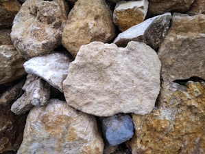 A collection of variously sized, rough-hewn stones stacked together. The stones vary in color from light beige to darker browns and grays, creating a textured surface.