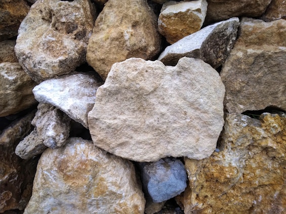 A collection of variously sized, rough-hewn stones stacked together. The stones vary in color from light beige to darker browns and grays, creating a textured surface.
