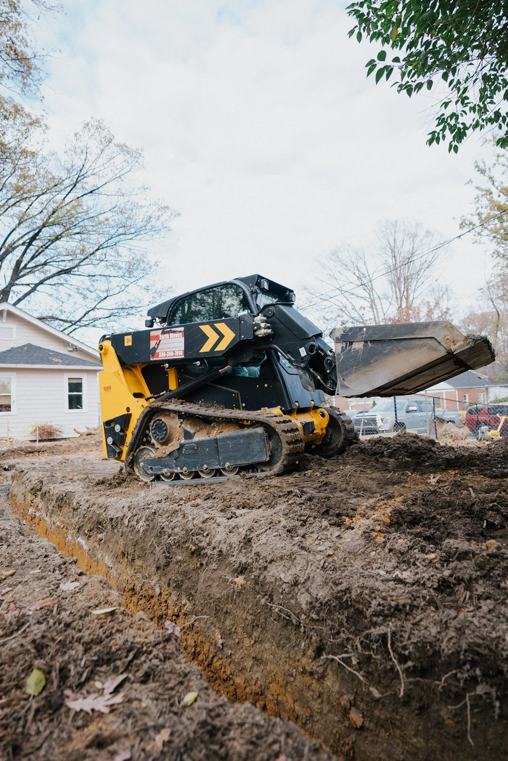 Track loader shaping soil alongside a house during a residential grading project