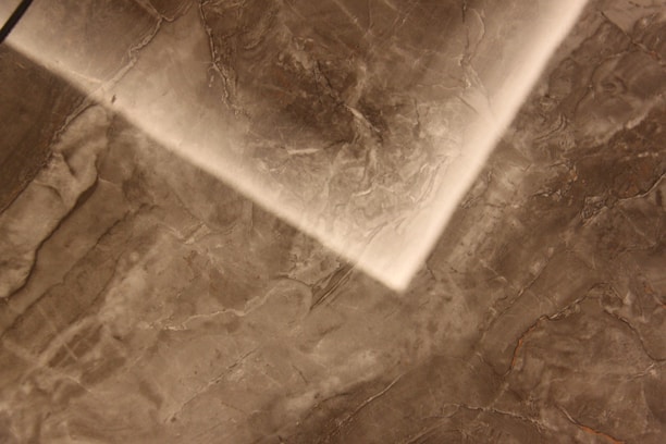 A close-up view of a textured marble or stone surface with a mix of dark and light brown shades. The surface features natural veining patterns and variations in color, creating an abstract, earthy look.