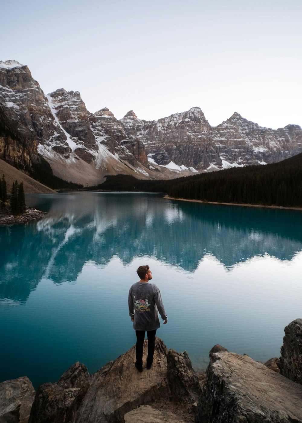 a man standing on a rock looking at a lake with mountains in the background