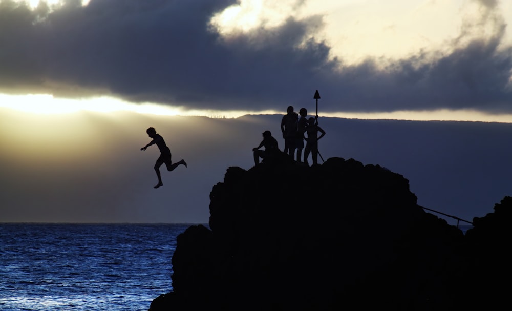 a group of people jumping off a cliff into the water