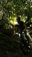 A person wearing a helmet is riding a fat-tire bike through a dense, leafy forest. The sunlight filters through the trees, casting dappled light on the ground and creating a serene, adventurous atmosphere.