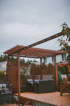 A beautifully crafted wooden pergola with string lights over a cozy backyard seating area at dusk.
