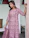 Portrait of a happy woman wearing a soft blush pink custom dress, smiling warmly in a boutique setting.