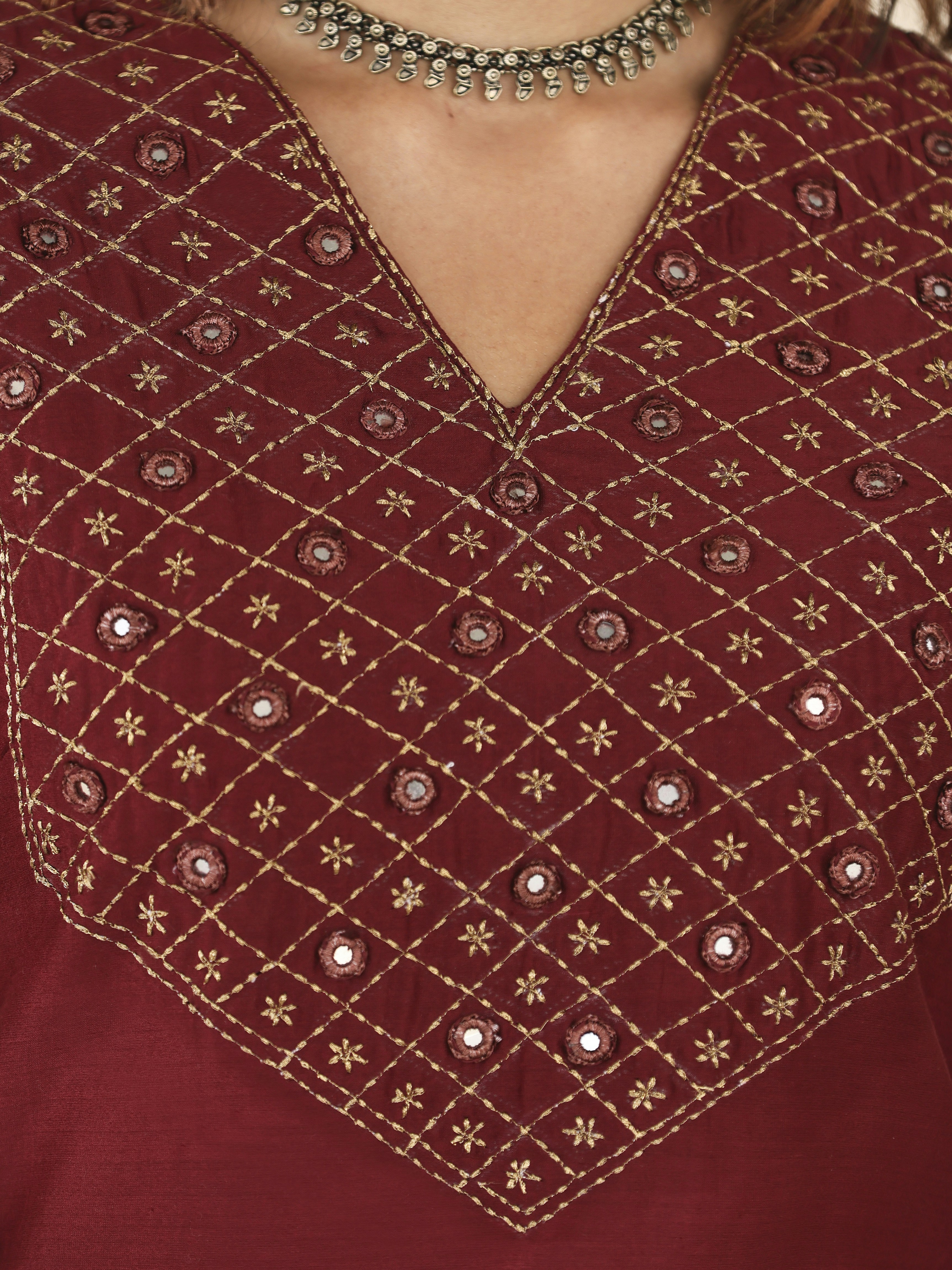 Intricate gold embroidery and mirrors on a red tunic neckline.