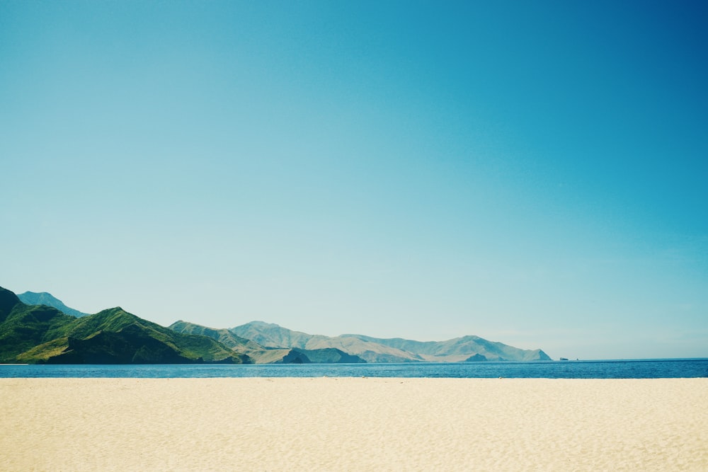 a beach with a body of water and mountains in the background