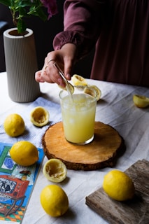 a person pouring a drink into a glass with lemons on a table