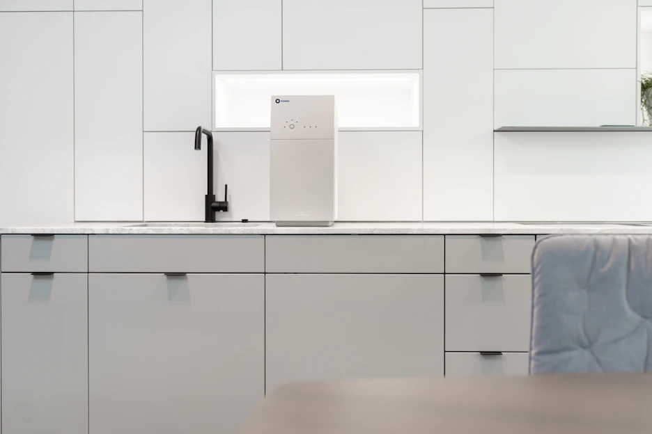 A sleek kitchen countertop featuring a modern under-the-sink reverse osmosis water filter with a glass of crystal-clear water beside it.