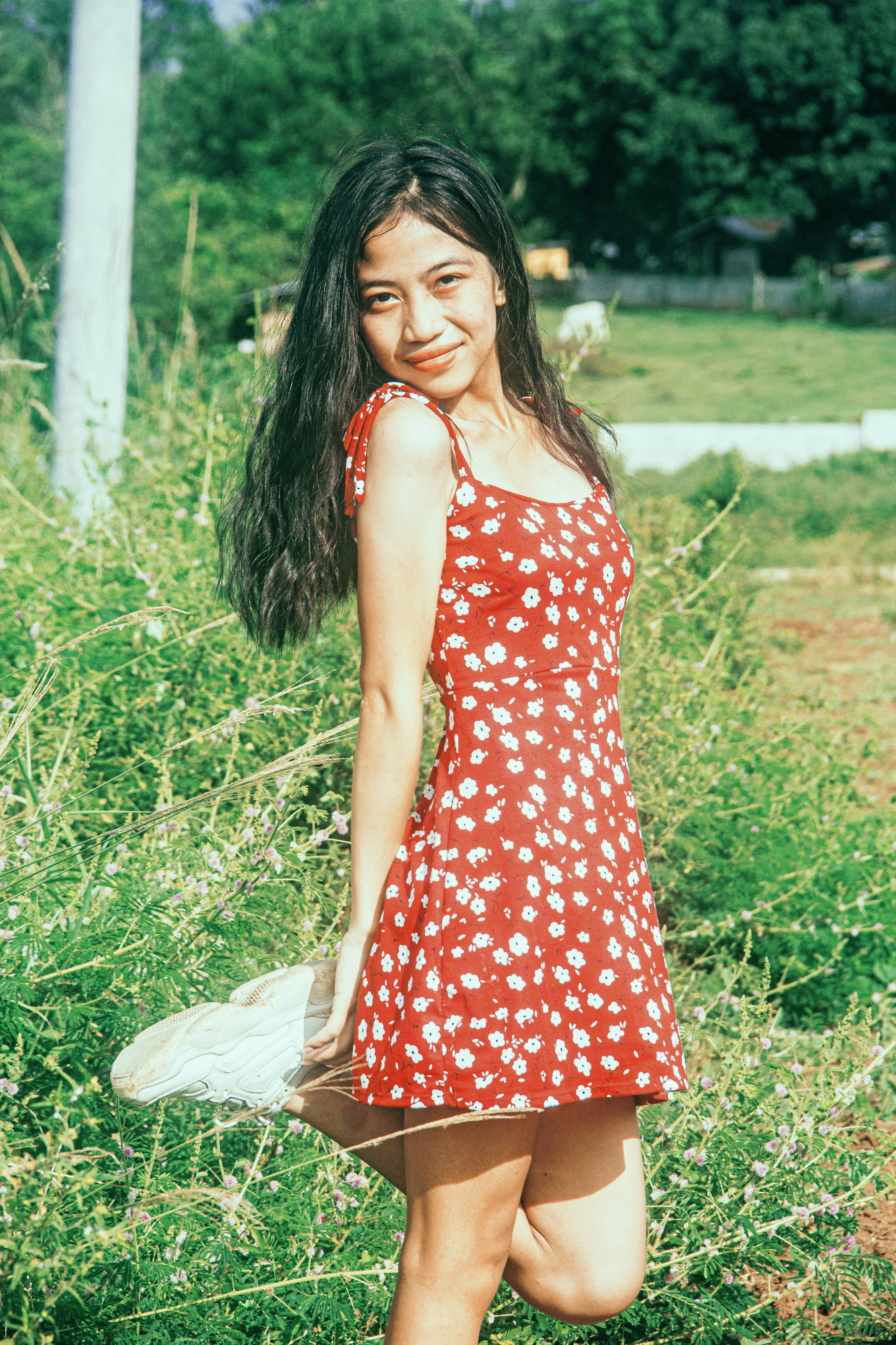 Young woman in floral wrap mini dress smiling outdoors, bright summer day, vibrant colors
