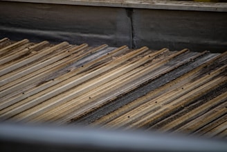 A corrugated metal roof with a slightly weathered and rusty appearance. The metal sheets are arranged in parallel lines, creating a textured pattern across the surface.