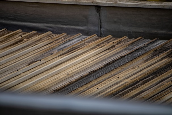 A corrugated metal roof with a slightly weathered and rusty appearance. The metal sheets are arranged in parallel lines, creating a textured pattern across the surface.