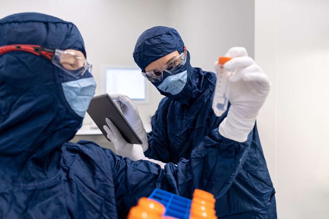 a few people in surgical scrubs and masks using a tablet, Laboratory technicians checking test tube