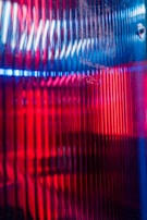 Bright, vertical lines of red and blue light create an abstract pattern on a textured surface. The optical illusion formed by the lines gives a sense of depth and movement.