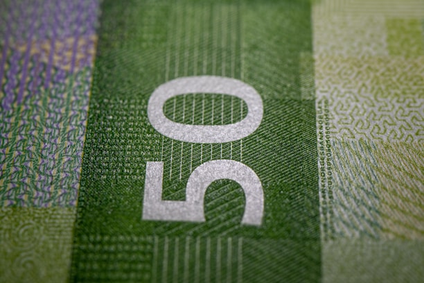 A close-up of a banknote featuring the number 50 prominently in white against a green patterned background. The texture is detailed with various shades and patterns that suggest security features.