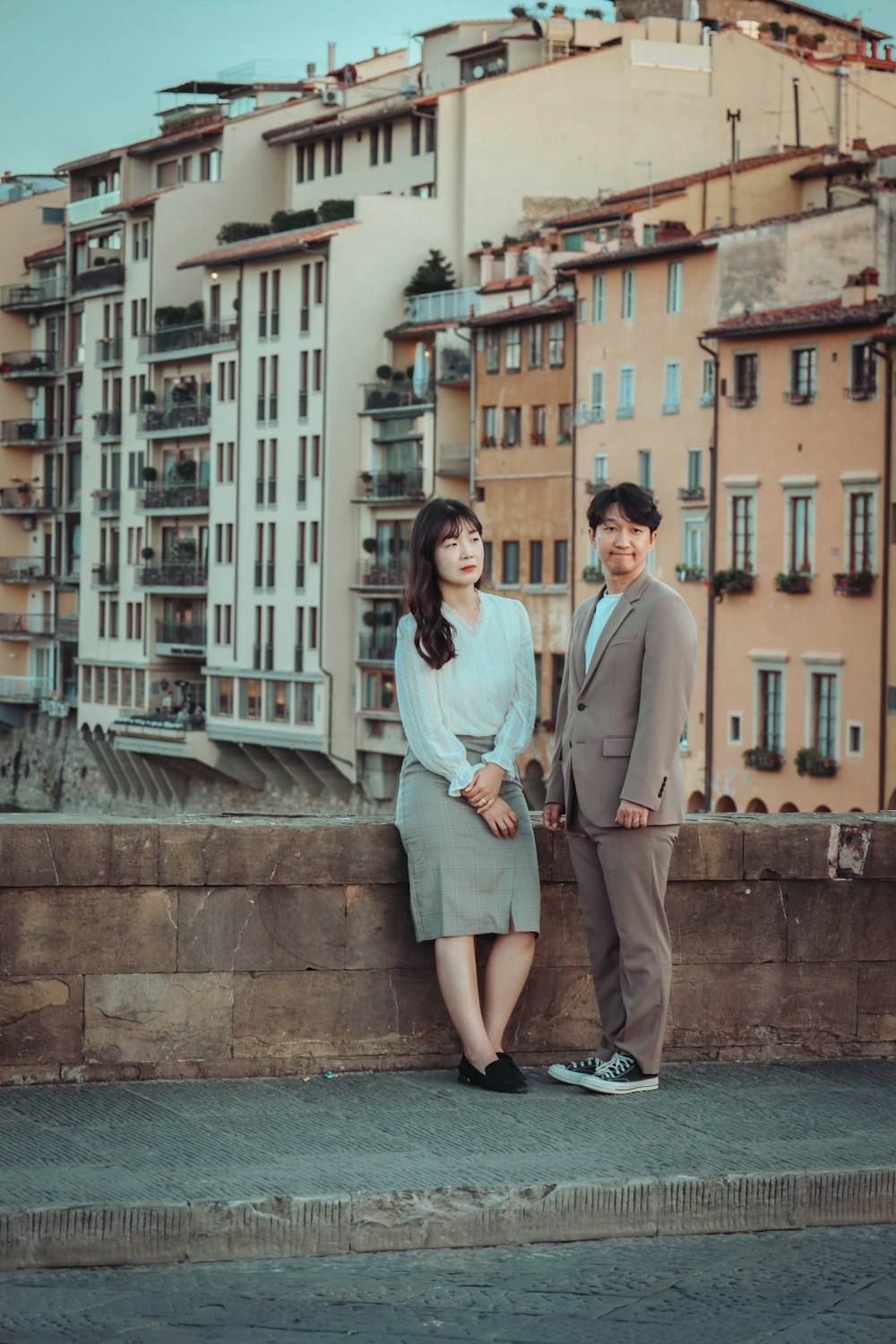 a man and woman posing for a picture in front of a row of buildings