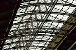 A complex and intricate metal framework forming an overhead structure, featuring interlocking beams and girders. The design conveys a sense of architectural strength and industrial sophistication.