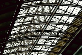 A complex and intricate metal framework forming an overhead structure, featuring interlocking beams and girders. The design conveys a sense of architectural strength and industrial sophistication.