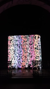 A large digital display showcases a vibrant and colorful pattern of abstract shapes resembling flowers or coral. The display is set within a dark space bordered by ornate, black wrought iron gates on either side.