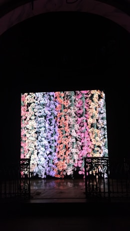 A large digital display showcases a vibrant and colorful pattern of abstract shapes resembling flowers or coral. The display is set within a dark space bordered by ornate, black wrought iron gates on either side.