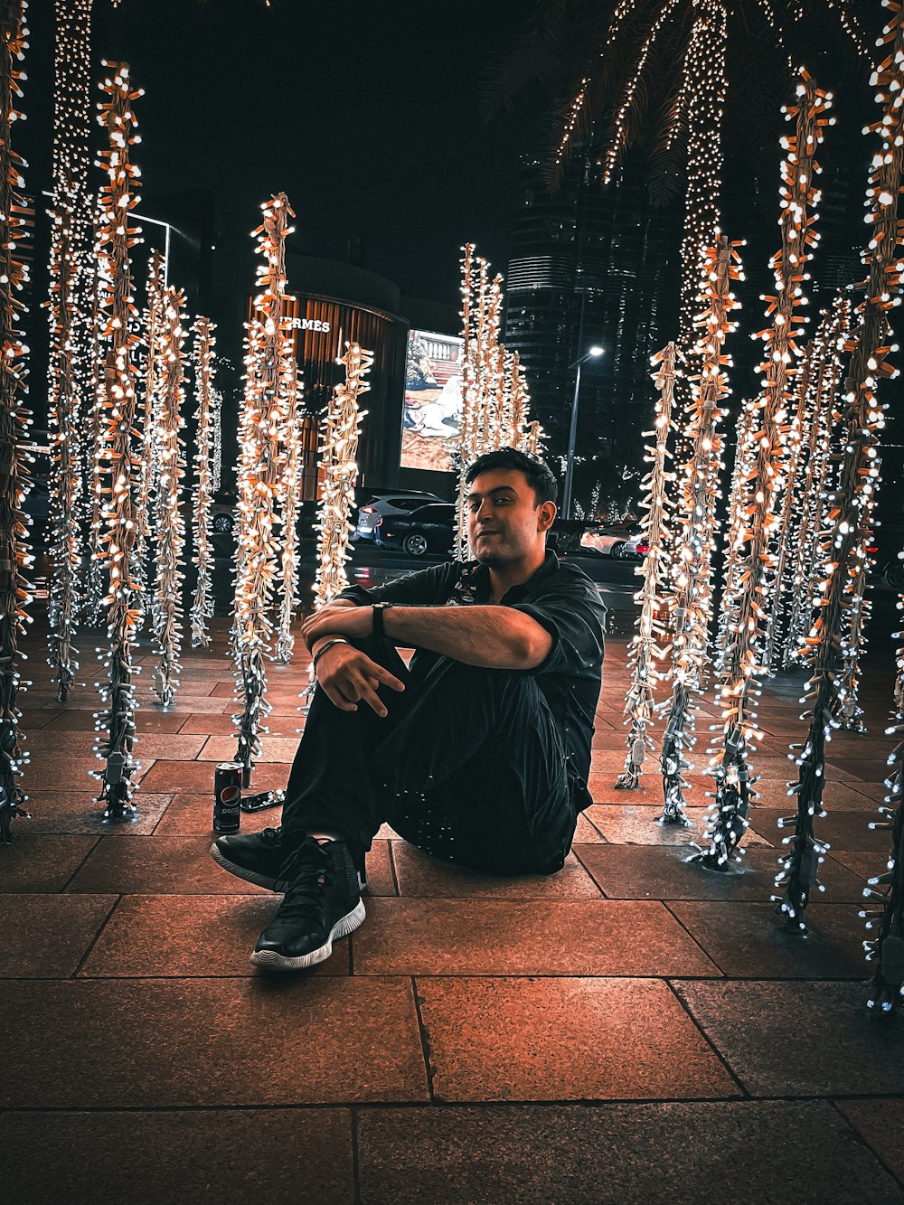 a person sitting on a sidewalk with christmas lights