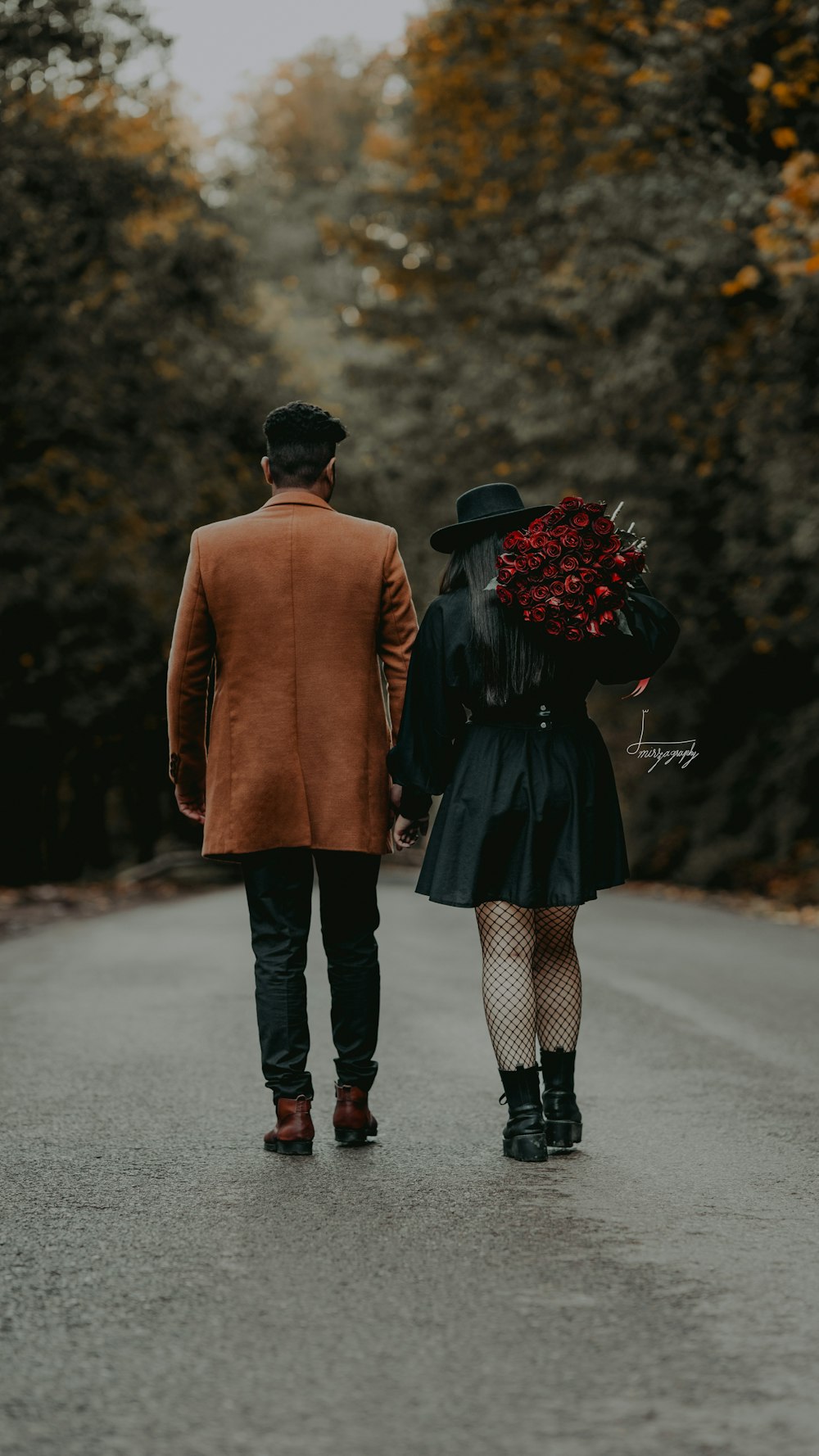 a man and woman walking down a road with trees on either side