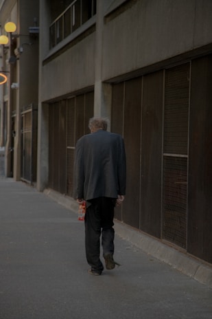 A lone figure in a futuristic cloak walking through a neon-lit alley, shadows dancing on rain-soaked pavement.
