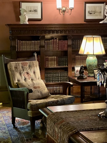 A plush velvet armchair beside a tall bookshelf filled with leather-bound volumes, under a soft spotlight.