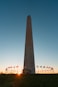 a tall monument with flags around it with Washington Monument in the background
